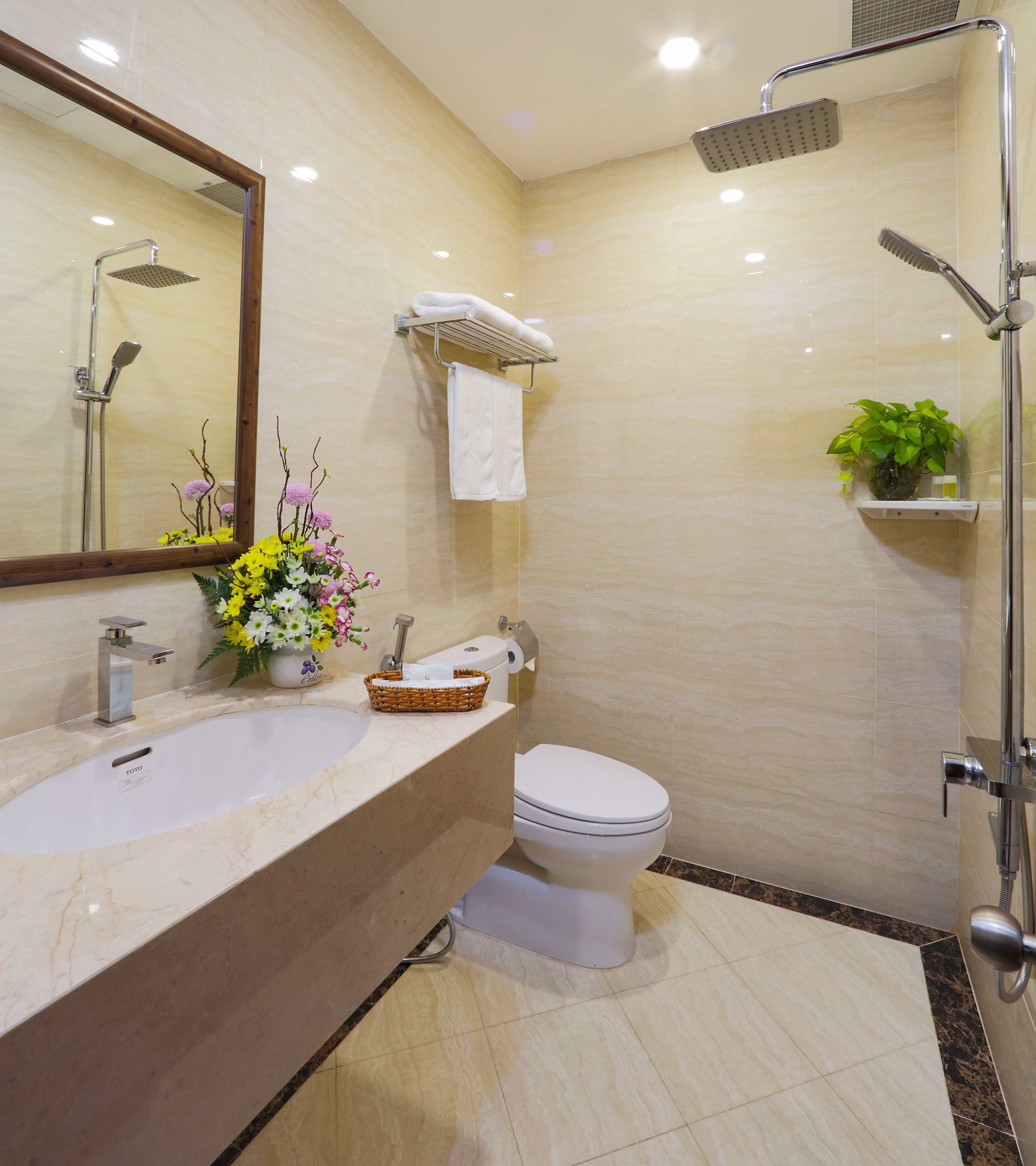 A modern bathroom with a sink, mirror, toilet, shower, and a potted plant.