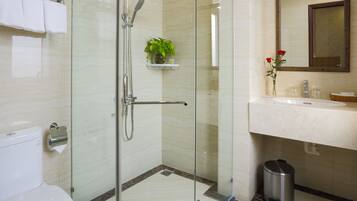 Un baño moderno con ducha de vidrio, inodoro, lavamanos con espejo y un cubo de basura.