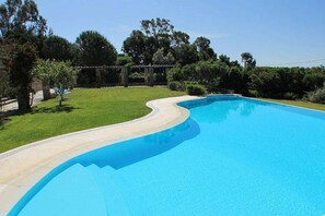 A swimming pool with a curved edge, surrounded by a grassy lawn and trees. - Villa Malveira - Style and Tradition in Portugal (Janes)