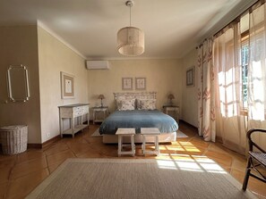A bedroom with a bed, bedside tables, a lamp, a chair, a hanging light fixture, and a window with curtains. - Villa Malveira - Style and Tradition in Portugal (Janes)