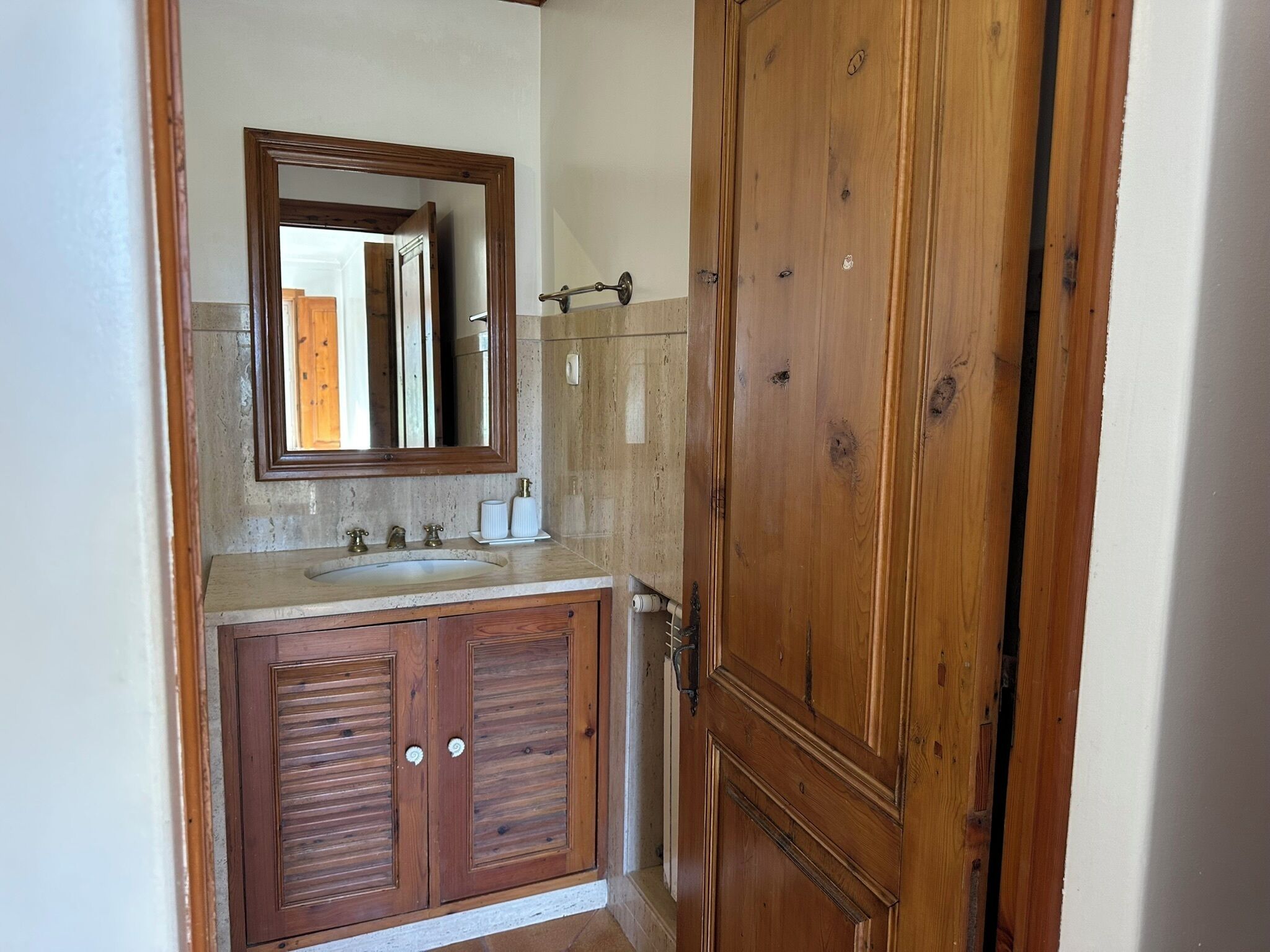 A bathroom with a wooden vanity, a mirror, a sink, and a door.