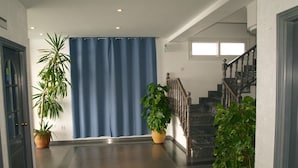 Un hall d’entrée spacieux, avec un rideau bleu, un escalier en bois et des plantes en pot.