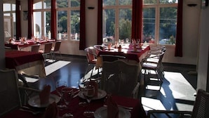 Un espace repas avec des tables dressées pour les repas, de grandes fenêtres et une vue sur les arbres.