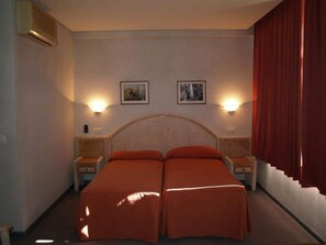 Habitación de hotel con cama doble, dos mesitas de noche, dos lámparas de pared y dos cuadros enmarcados.
