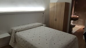 A small, single-bed room with a wooden wardrobe and a bathroom visible through an open door. - Mansion Alba "a dream" (Alcaudete)