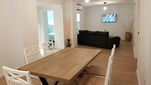 A dining area with a wooden table and white chairs, a black sofa, and a TV mounted on the wall. - Mansion Alba "a dream" (Alcaudete)