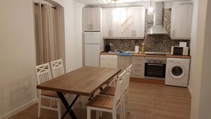 A compact kitchen with white cabinets, a wooden dining table, and a washing machine. - Mansion Alba "a dream" (Alcaudete)