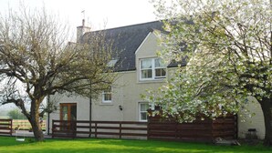 A two-story house with a sloped roof, a front door, and a small porch. - A Beautiful Rural Farmhouse With Flexible Living Space And Great Views (Stirling)