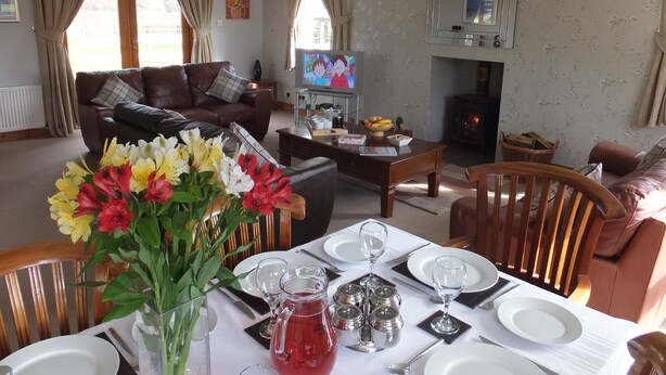 A living room with a fireplace, a television, and a dining area set for a meal. - A Beautiful Rural Farmhouse With Flexible Living Space And Great Views (Stirling)