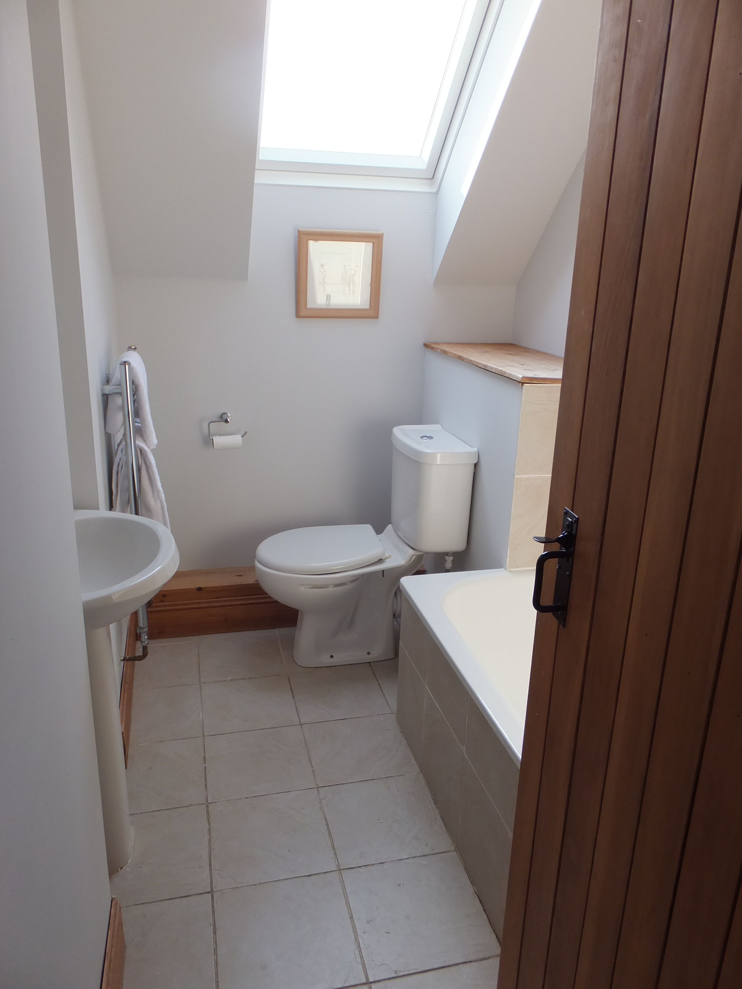 A compact bathroom with a skylight, a toilet, a sink, and a bathtub.