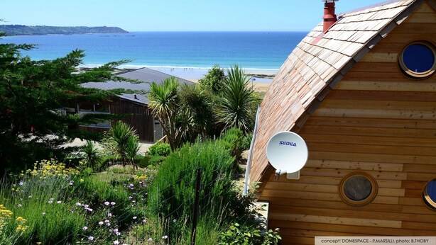 Una casa de madera con antena parabólica, con vista a una playa y al océano.