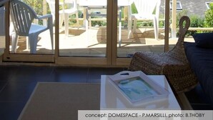 Una habitación con un amplio ventanal corredizo que da a un área de estar al aire libre con vista al mar.