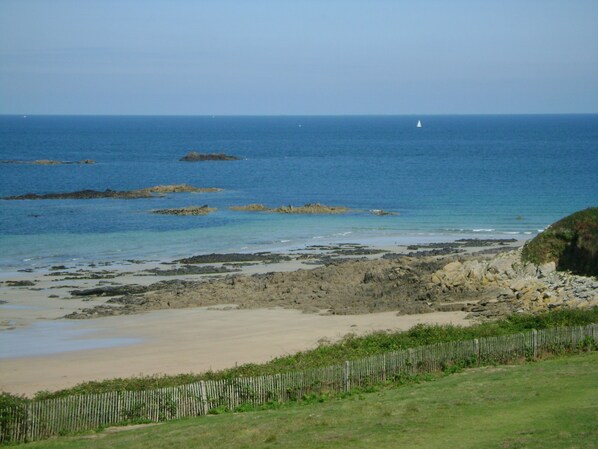 A coastal landscape with rocky shores, a sandy beach, and a grassy area with a wooden fence.