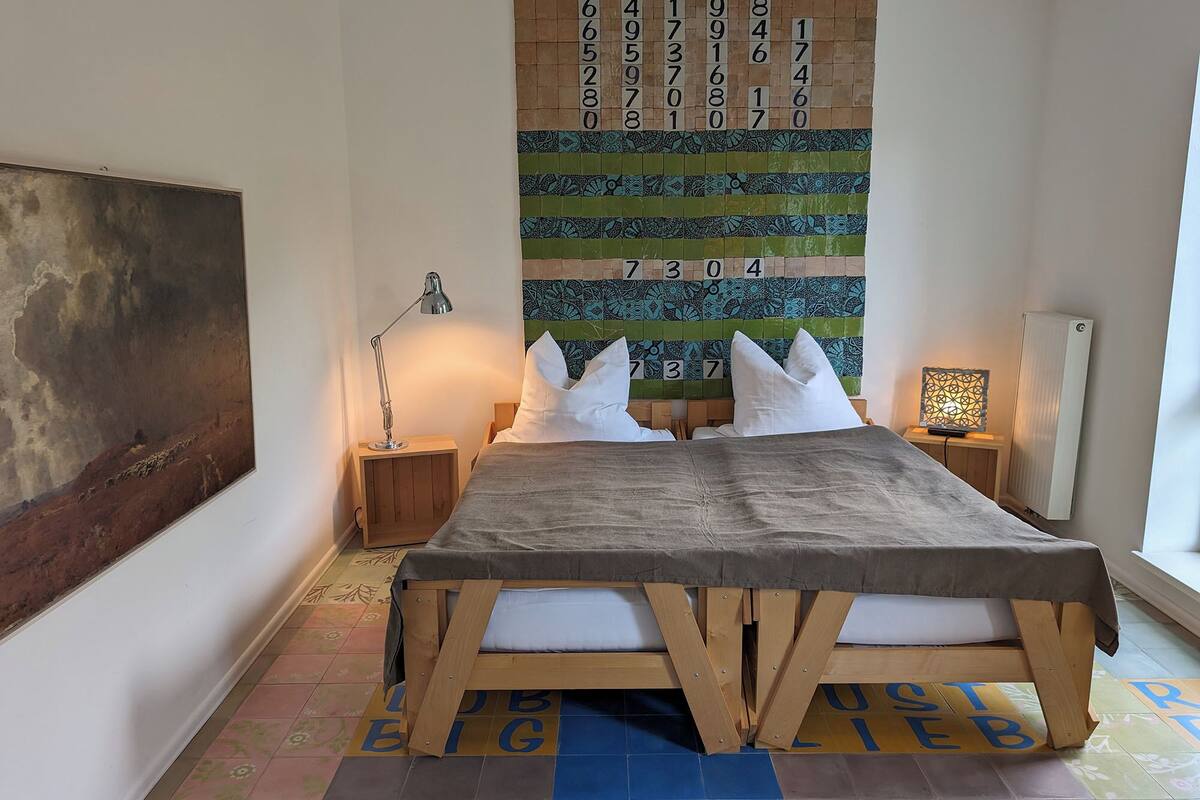 A bedroom with a bed, two bedside tables, a lamp, a wall tapestry, and a radiator.