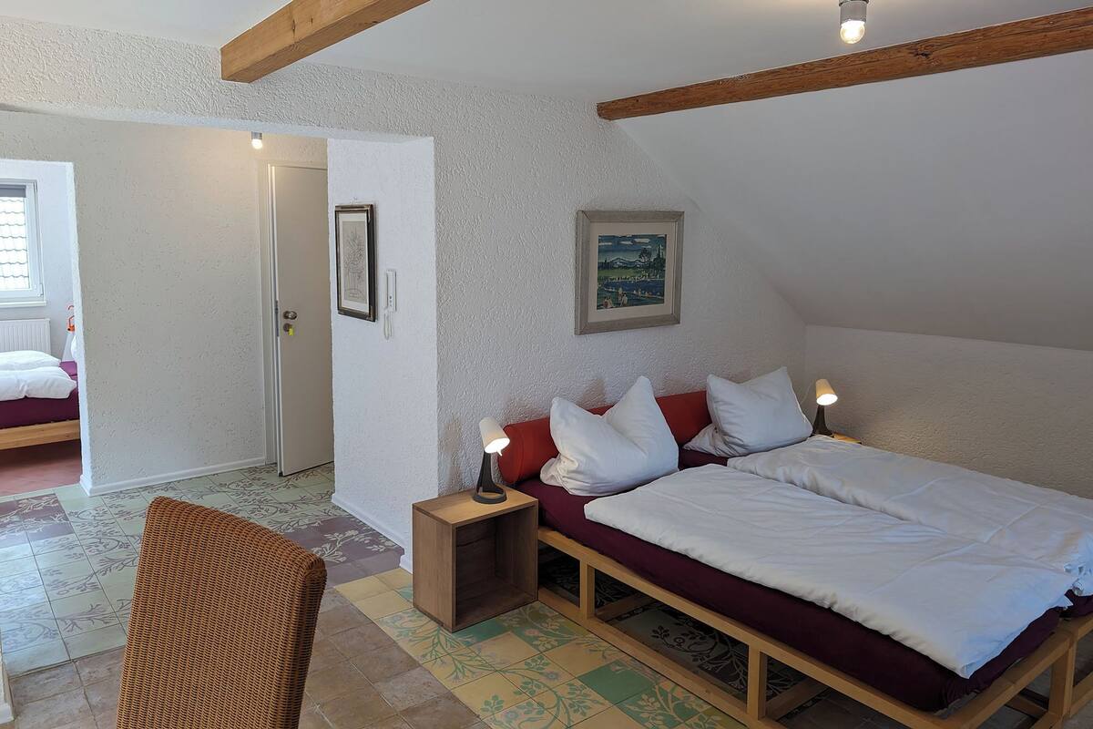 A bedroom with a bed, a nightstand, a chair, and a door leading to another room.