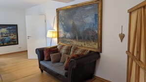 A room with a dark leather sofa, a large framed painting, a lamp, and a wooden cabinet. - Loreley Guesthouses (Sankt Goar)
