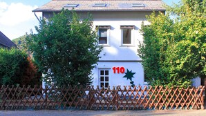 A white building with the number 110 on the facade, surrounded by a wooden fence and trees. - Loreley Guesthouses (Sankt Goar)