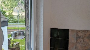 A room with a window overlooking a green landscape and a tiled fireplace. - Loreley Guesthouses (Sankt Goar)