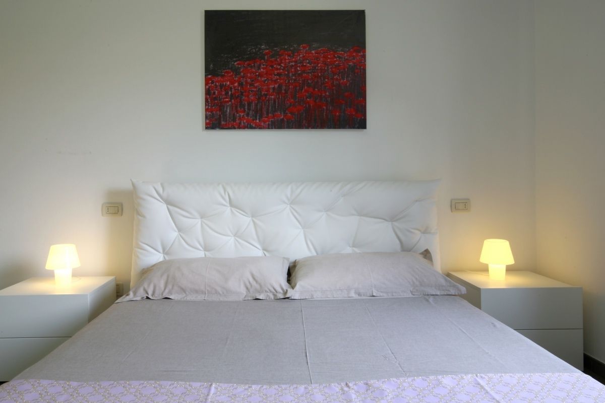 A neatly made bed with a tufted headboard, two bedside tables with lamps, and a painting of red flowers on the wall.