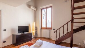 A bedroom with a bed, a TV, a radiator, a window, and a wooden staircase. - Apartment to rent in via Venezia in Florence by Mmega (Firenze)