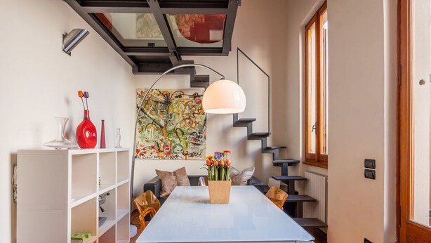 A modern dining area with a white table, wooden chairs, a pendant light, and a staircase. - Apartment to rent in via Venezia in Florence by Mmega (Firenze)