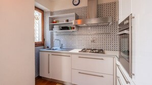 A kitchen with white cabinets, a stainless steel range hood, a gas stove, and a clock on the wall. - Apartment to rent in via Venezia in Florence by Mmega (Firenze)
