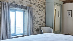 Une chambre avec des murs en pierre, un plafond en bois, un lit, une armoire et une fenêtre avec des rideaux.