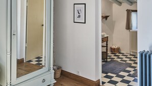 Une pièce avec une armoire blanche, un sol à carreaux, un tableau encadré au mur et une fenêtre avec des rideaux.