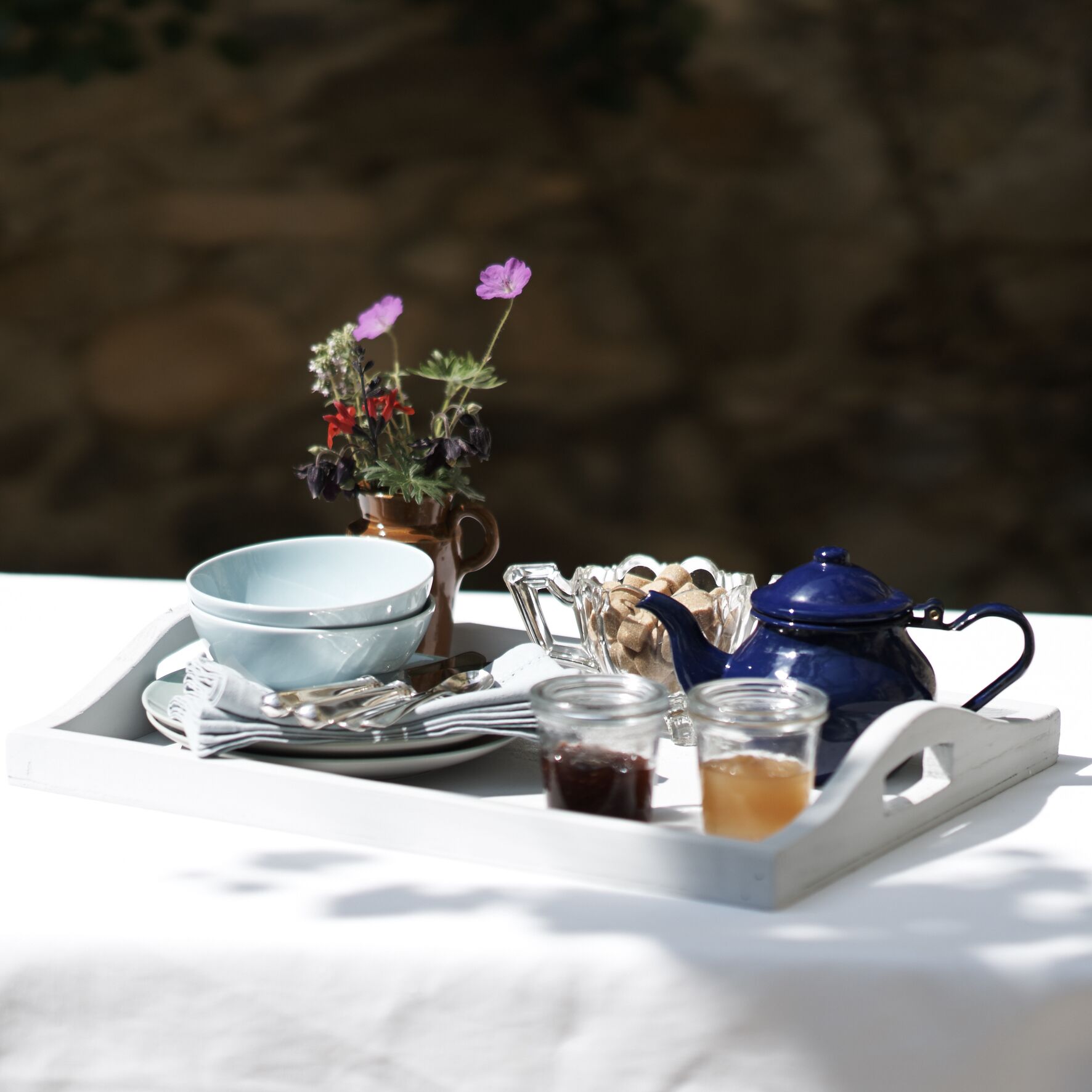 A tray with a blue teapot, a white bowl, a glass pitcher, and two small glasses with tea.