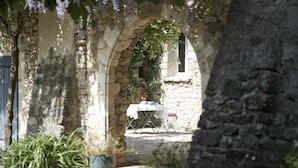 Un espace de restauration en plein air, avec une table et des chaises placées sous une arche, le tout entouré de murs en pierre et de plantes en pot.