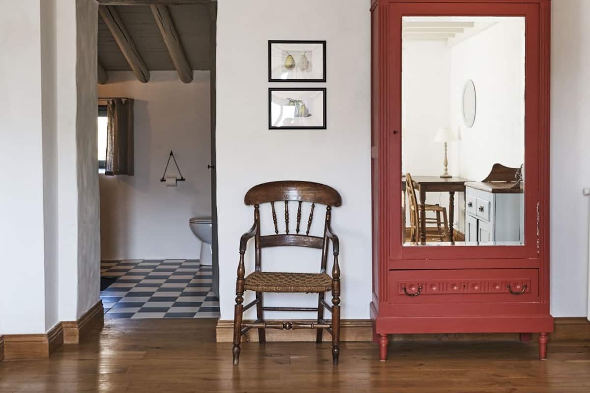 A room with a wooden floor, a red cabinet with a mirror, a wooden chair, and a checkered floor.