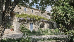 Un bâtiment en pierre avec un jardin à l’avant, agrémenté d’un mur en pierre, de plantes en pot et de plantes grimpantes.