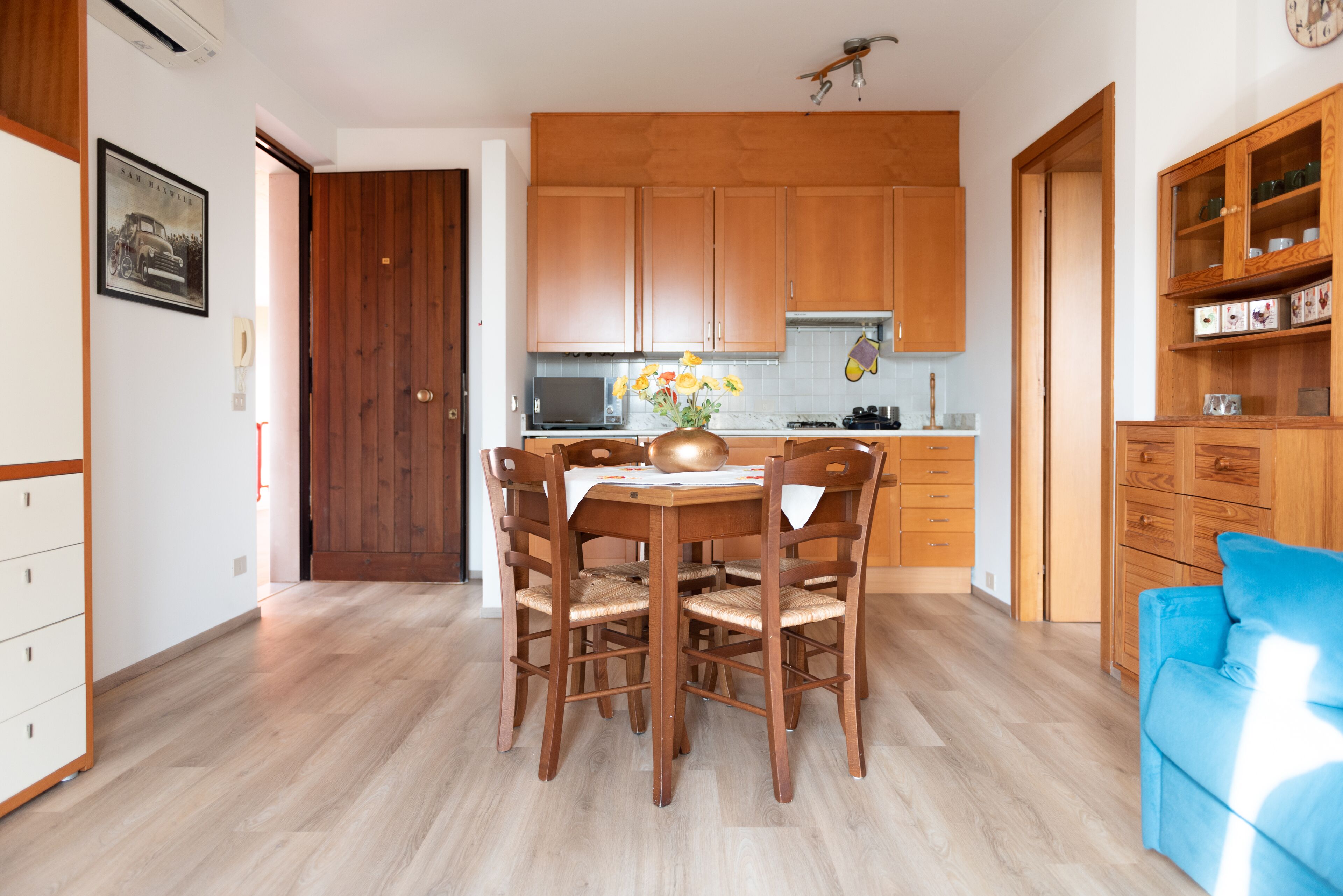A modern kitchen with wooden cabinets, a dining table with chairs, and a blue sofa in the living area.