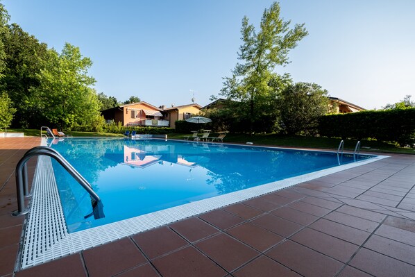 A rectangular swimming pool with a metal ladder on the left, surrounded by a tiled deck.