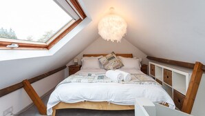 Een knus zolderkamer met een dakraam, een pluizige witte lamp en een net opgemaakt bed.