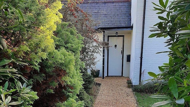Een houten bord met daarop 'Rose Cottage', wijzend naar een wit huis met een donker dak.