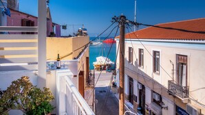 A narrow street with buildings on either side, a clear blue sky, and a view of the sea with boats. - The Roof - Flat Sea View in Aegina Town (Aegina)