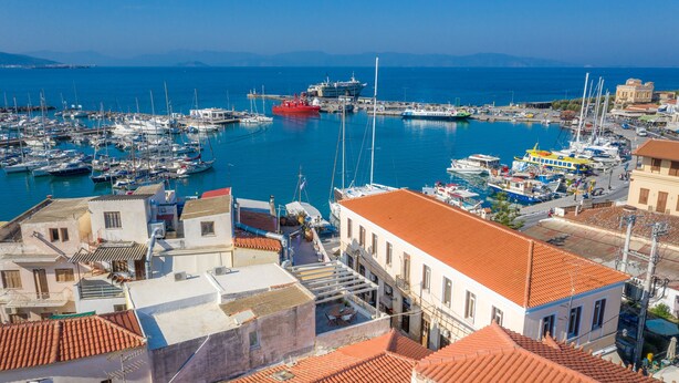 A marina with boats docked, buildings with red-tiled roofs, and a clear view of the sea and distant mountains. - The Roof - Flat Sea View in Aegina Town (Aegina)
