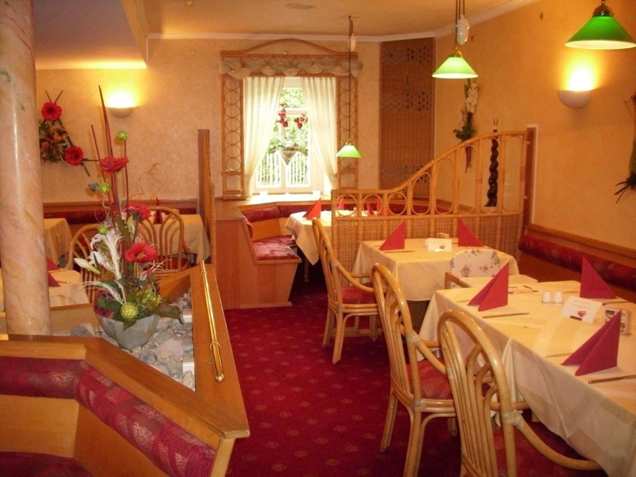 A restaurant with wicker furniture, a red carpet, and a window with curtains.