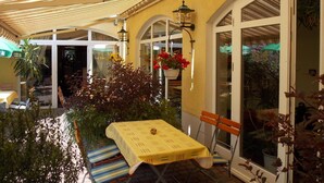 Un área de patio al aire libre con una mesa, sillas, una cesta de flores colgante y una lámpara.