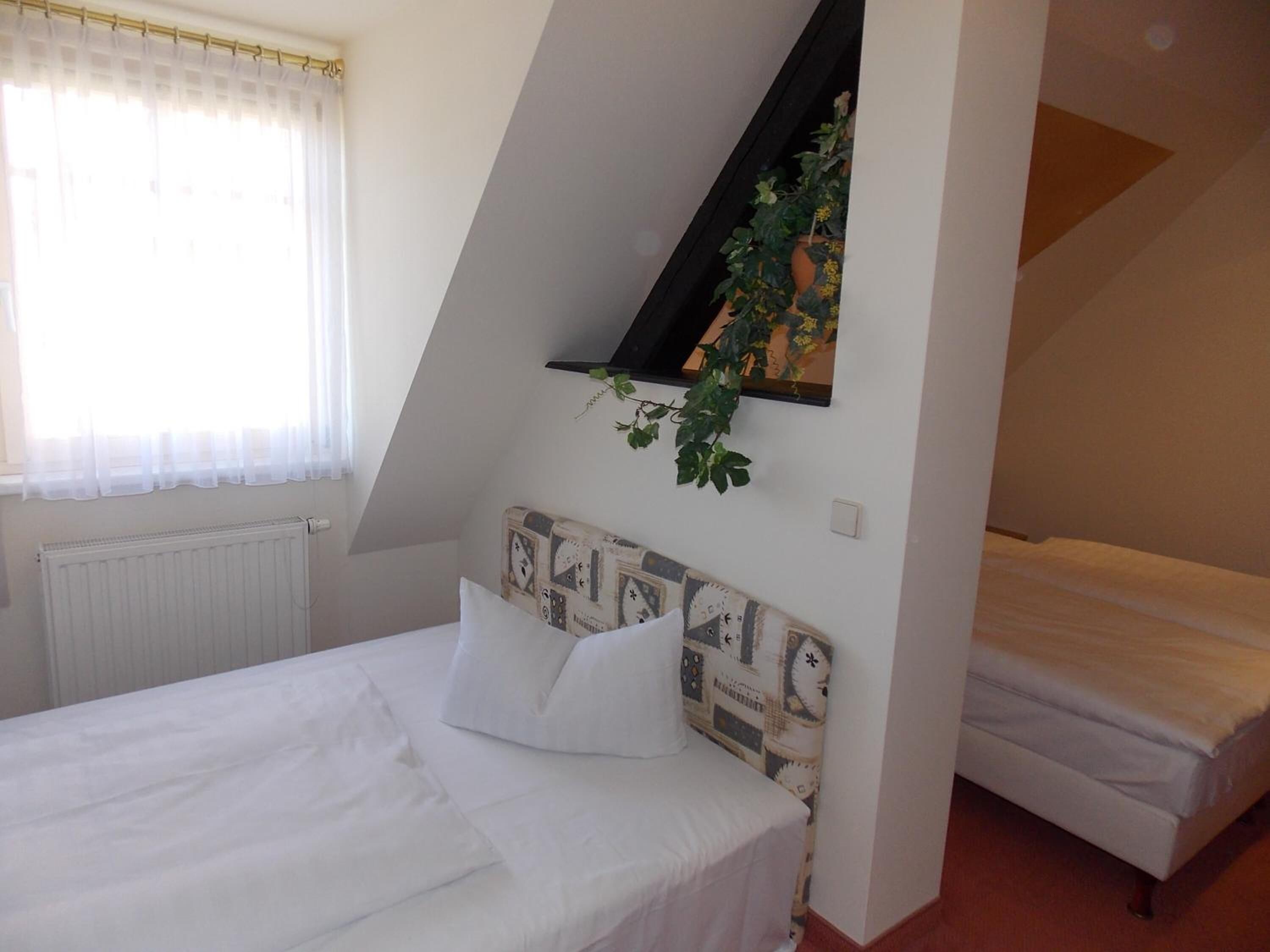 A bedroom with a single bed, a smaller bed, a radiator, and a window with sheer curtains.