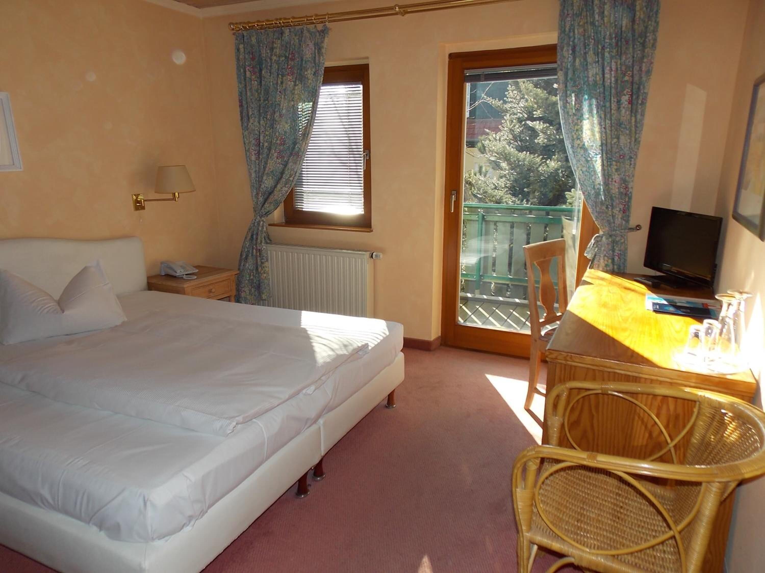 A hotel room with a bed, a desk with a chair, a television, and a window with curtains.