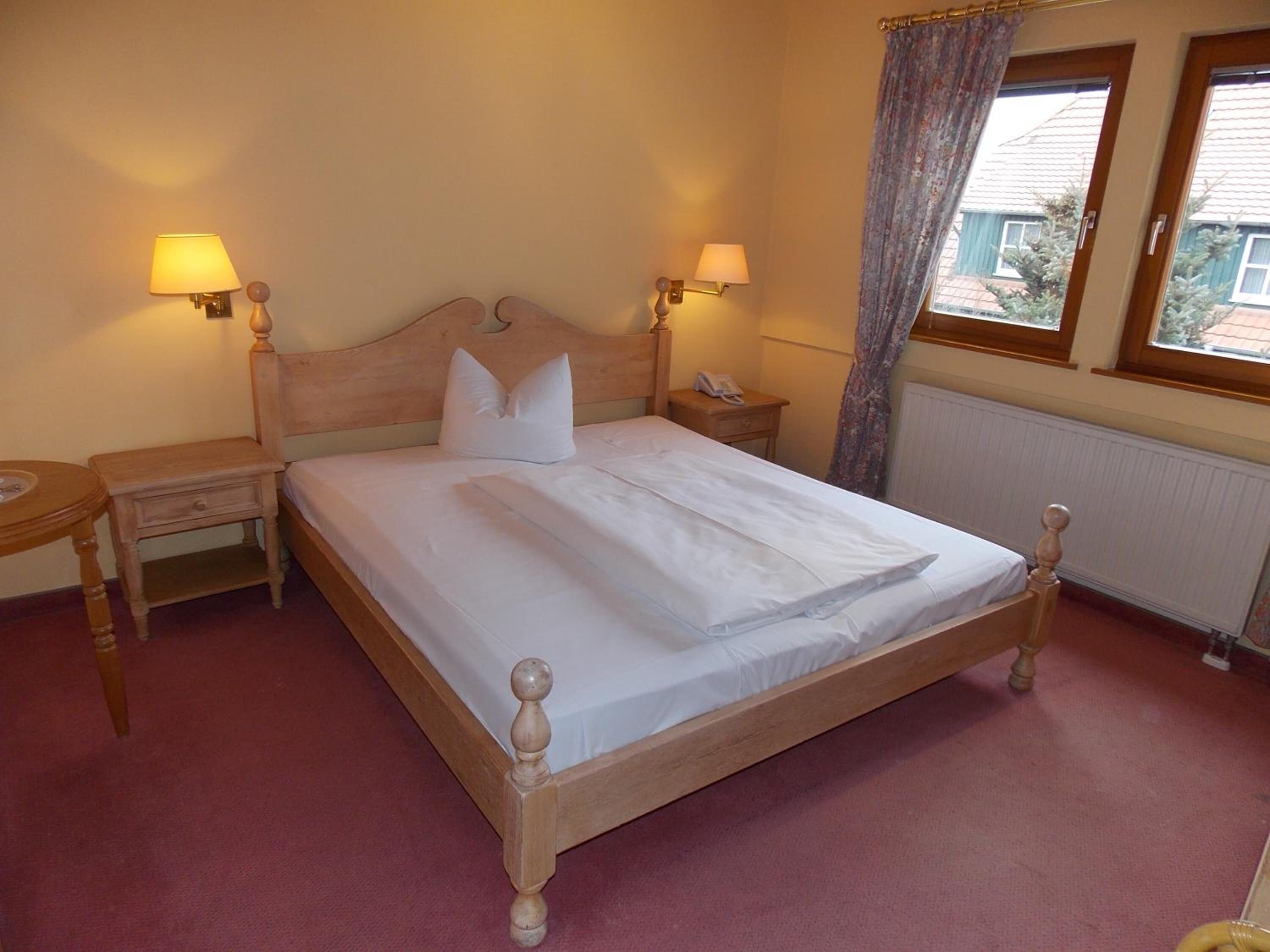 A neatly made bed with a wooden headboard, two bedside tables with lamps, and a window with curtains.