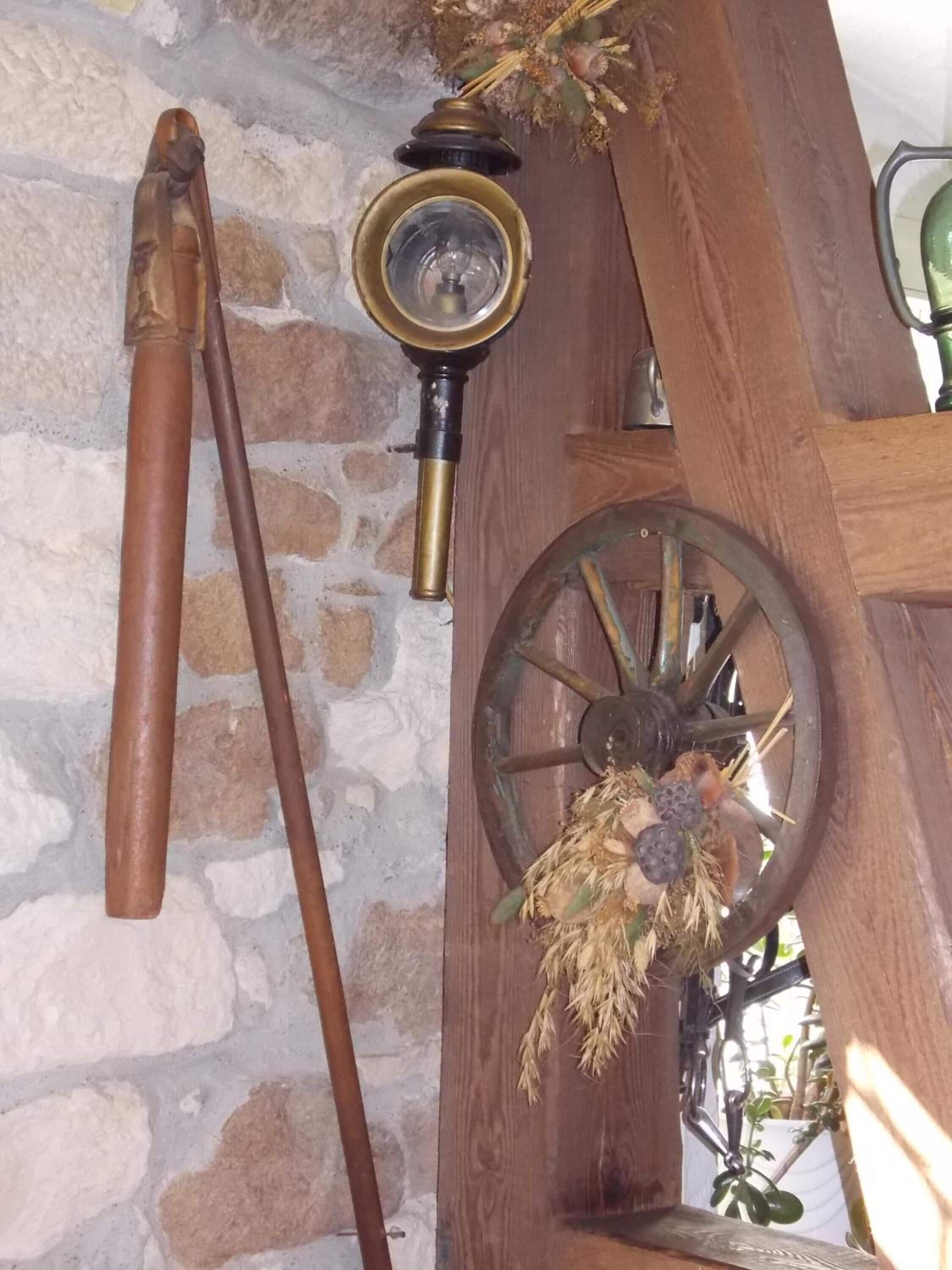 Un interior rústico con pared de piedra, viga de madera, farol de latón y una rueda decorativa.