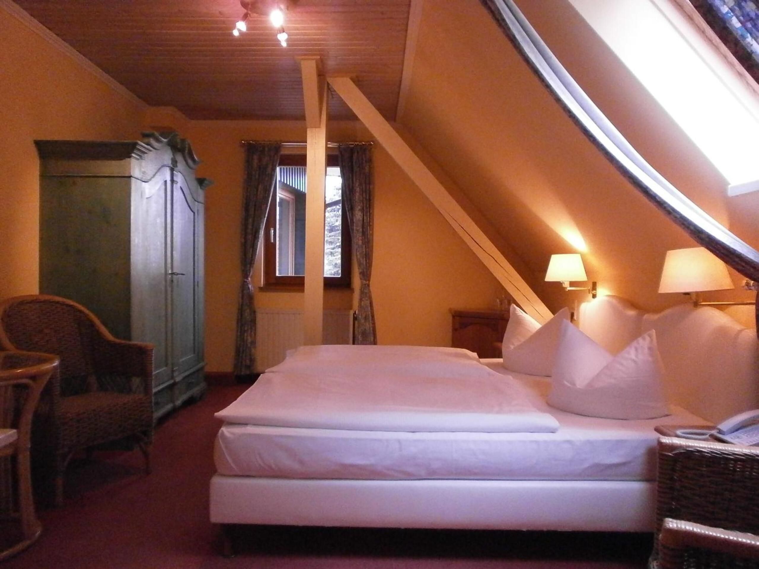 Un dormitorio con cama, una silla, un armario y una ventana con cortinas.