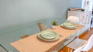Un coin repas avec une table en verre, des chaises blanches et un mur bleu clair.