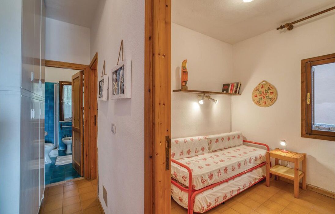 Una stanza compatta con un letto, un tavolino e uno scaffale con libri e oggetti decorativi.