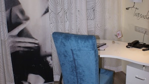 A room with a desk, a blue chair, a flat-screen TV, a patterned curtain, and a poster on the wall.