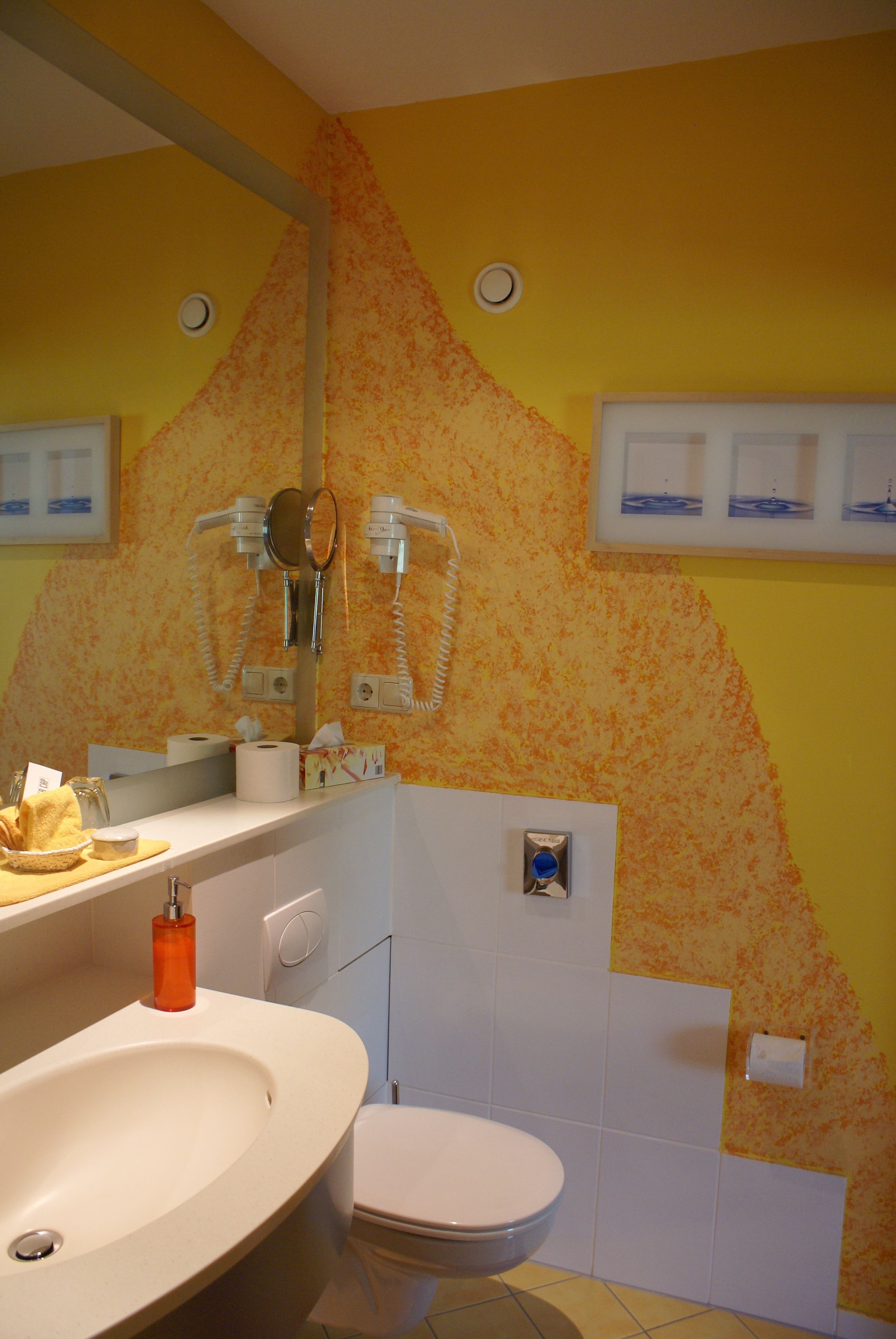 A bathroom with a yellow wall, a white sink, a toilet, and a mirror.