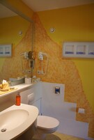 A bathroom with a yellow wall, a white sink, a toilet, and a mirror.